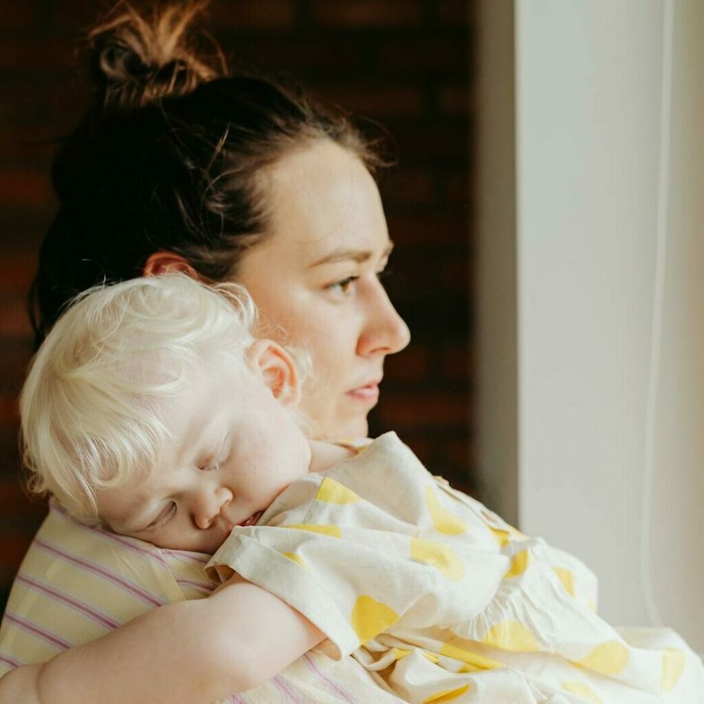 A mother lovingly holds her sleeping child as they gaze out the window, capturing a tender family moment.